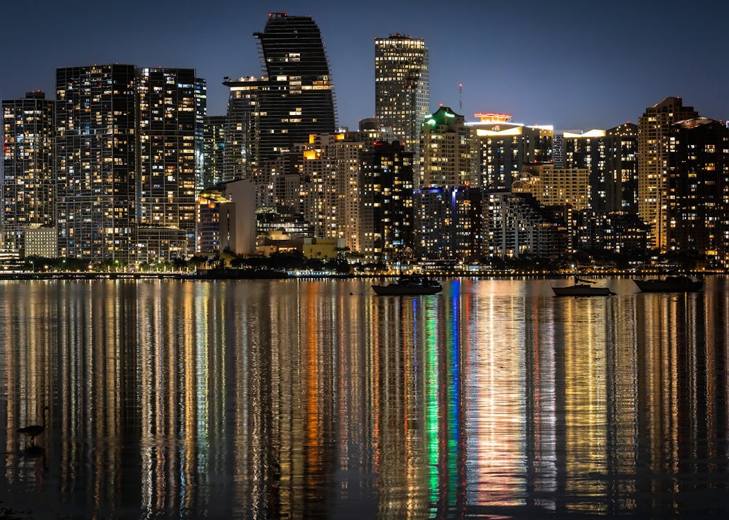 Skyline do centro de Miami iluminado à noite refletido sobre a Biscayne Bay, ilustrando o profundo estoque de condomínios acima de um milhão da região o ano inteiro