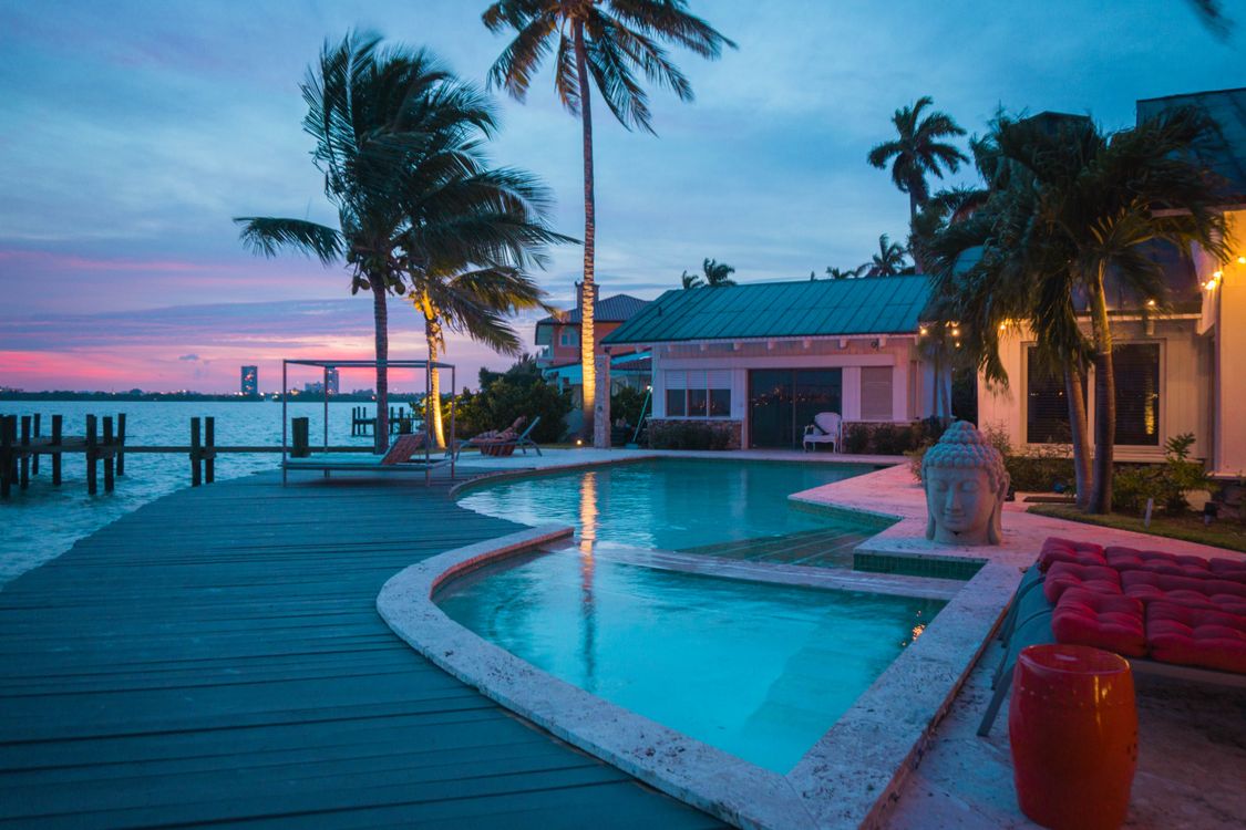 Casa unifamiliar frente al mar en Miami con piscina, muelle y palmeras al atardecer en Florida