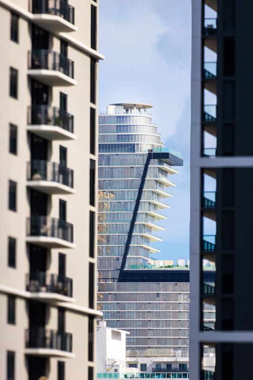 Uma torre de condomínios de luxo de vidro emoldurada entre dois edifícios residenciais em Miami, ilustrando o perfil de produto de marca e concluído que The Standard Residences oferece em Midtown