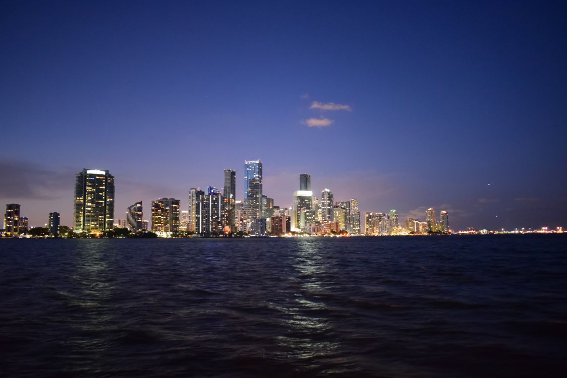Horizonte de Miami ao entardecer sobre Biscayne Bay, o mercado de luxo do Downtown e Brickell que atrai compradores da Califórnia que se realocam antes da votação do imposto sobre a riqueza de 2026