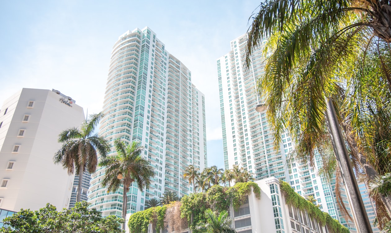Torres gêmeas de condomínios de luxo de vidro em Miami emolduradas por palmeiras, o tipo de produto de residências de marca que é vendido com um prêmio no mundo todo