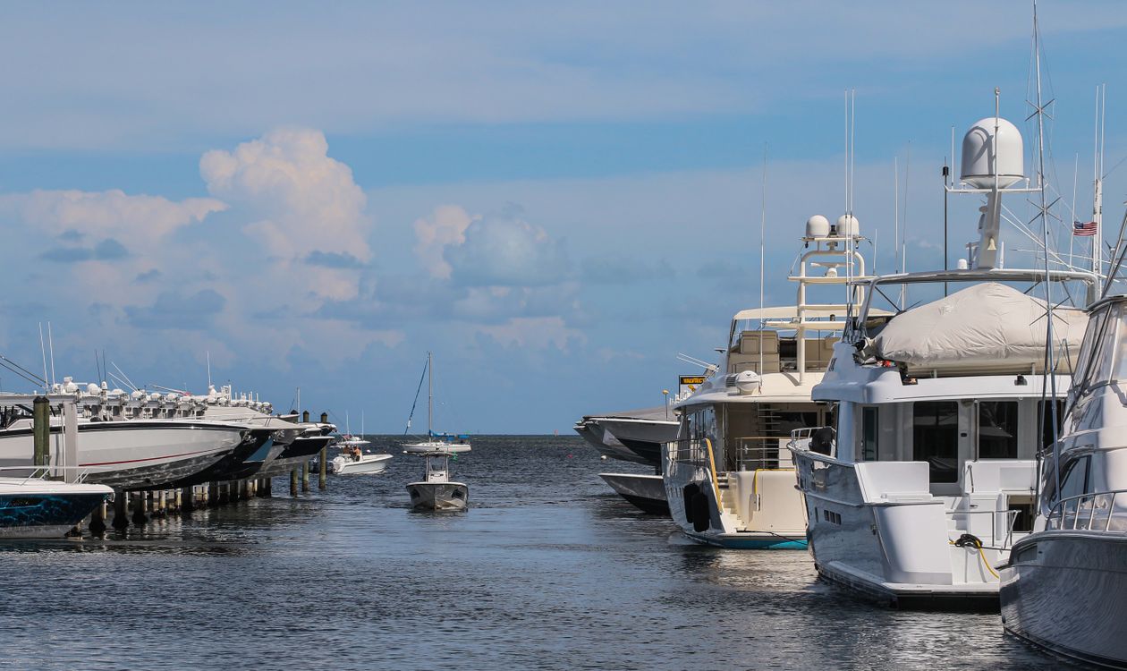 Grandes yates de lujo atracados en una marina de Miami con embarcaciones menores en elevadores al otro lado del canal