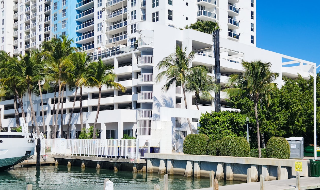 Prédio de condomínios à beira-mar em Miami com palmeiras e um iate atracado, o tipo de torre onde se combinam unidades em casas maiores