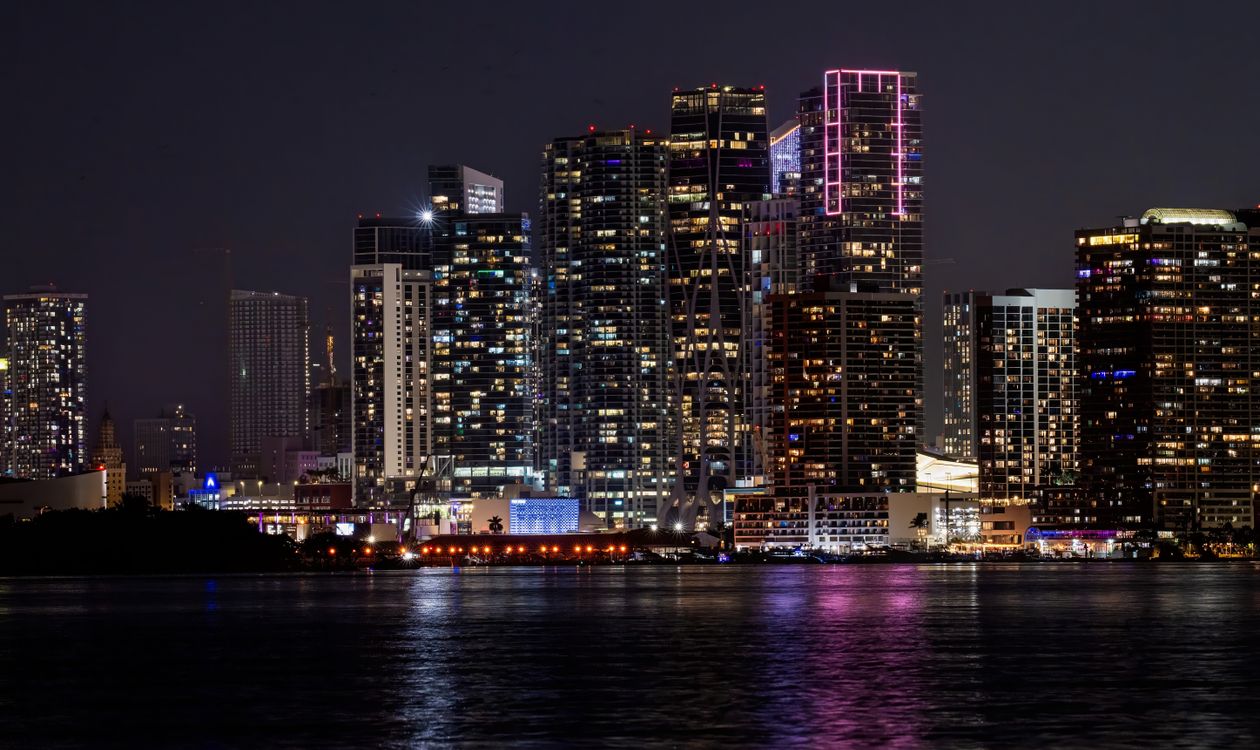 Horizonte iluminado de condomínios à beira da baía de Miami à noite visto da Baía de Biscayne