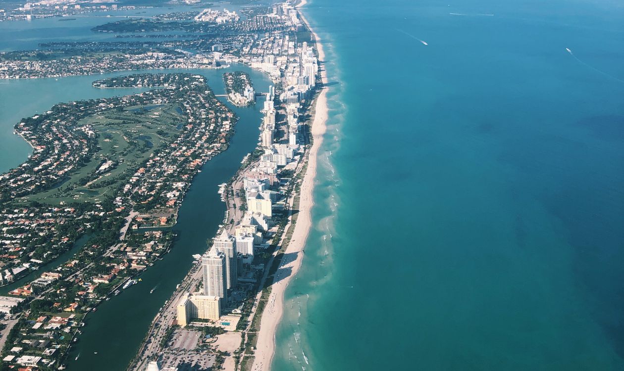 Aerial view of the Miami Beach barrier island and Atlantic coastline showing dense condominium development along the shoreline and bayfront estates on the inland side