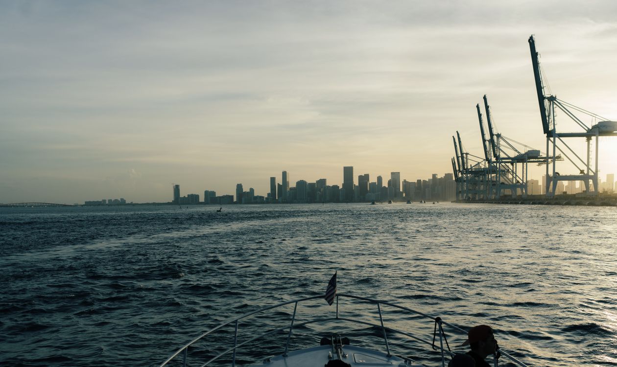 Downtown Miami condo skyline and Port of Miami gantry cranes seen from Biscayne Bay, the pre-construction market where developers now spend millions on sales galleries to sell unbuilt units
