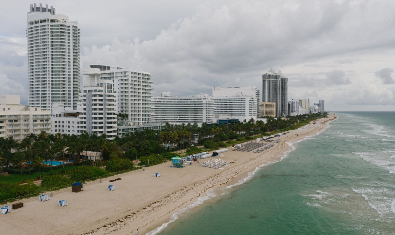 Oceanfront high-rise condominium buildings along the Miami Beach shoreline on an overcast day, showing the varied tower heights and setbacks that determine which units keep unobstructed water views