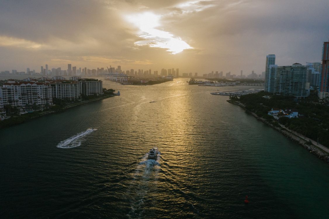 Vista aérea del canal entre Miami Beach y el perfil urbano del centro de Miami al atardecer, con torres de condominios en ambas orillas