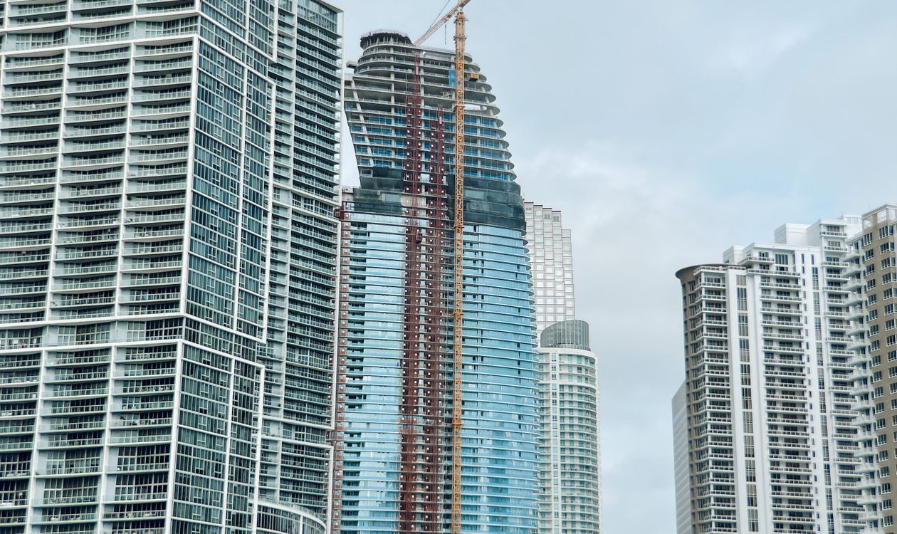 Una torre de condominios de Miami en construcción con una grúa amarilla, flanqueada por dos edificios residenciales ya terminados