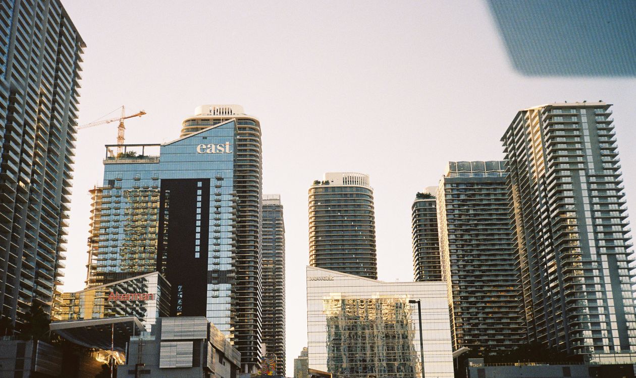 Torres de condominios de Miami al atardecer con una grúa de construcción elevándose detrás, la mezcla de oferta entregada y en obra que define el corredor de Edgewater y Brickell en 2026