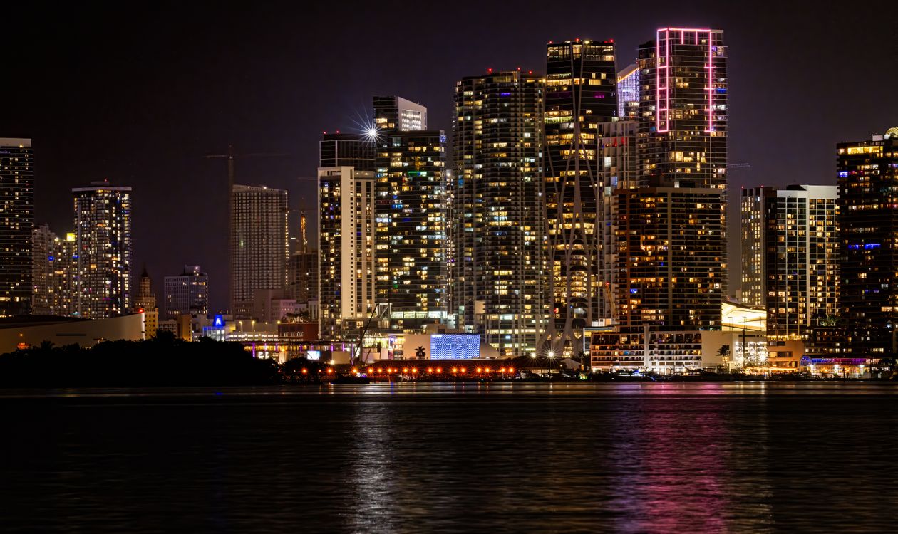 Torres de condominios frente a la bahía en Miami iluminadas de noche sobre Biscayne Bay, con una grúa de construcción entre ellas