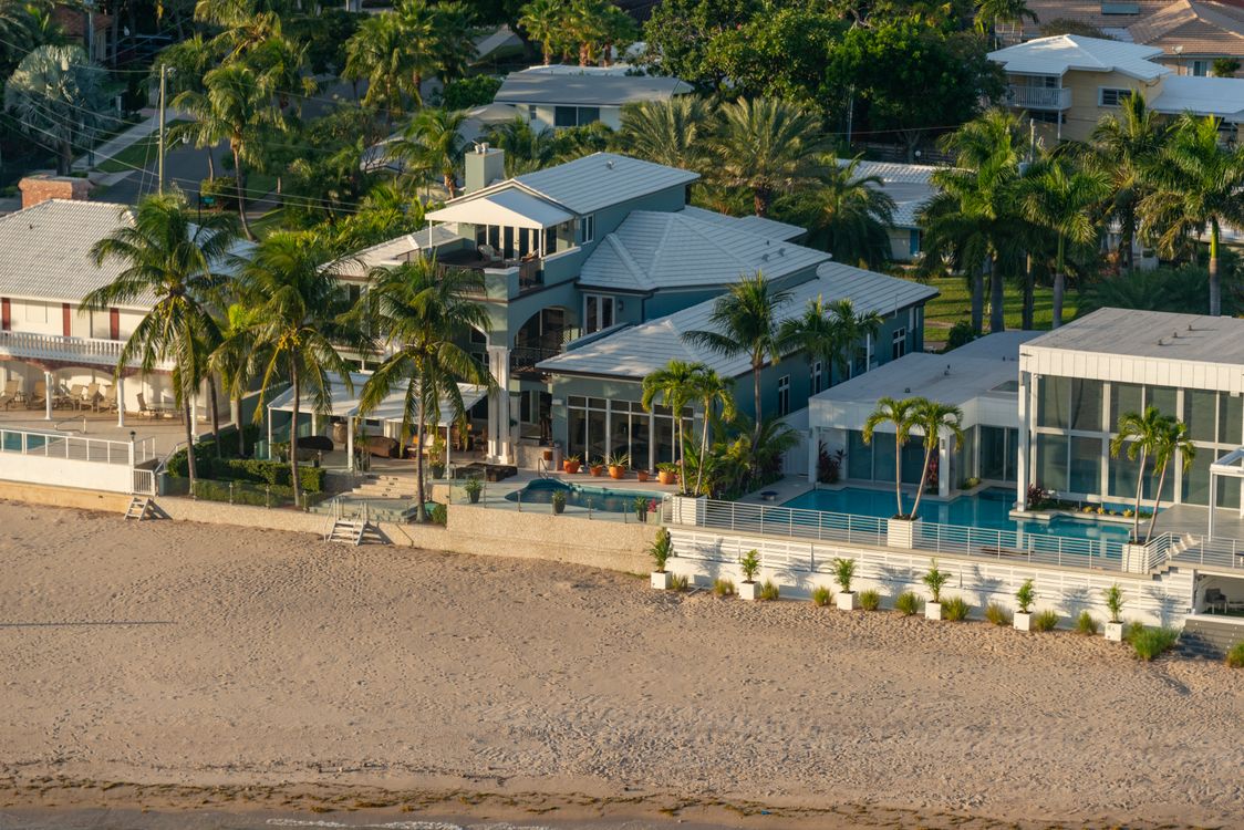 Aerial view of South Florida beachfront estates with private pools, palm trees and a seawall on the sand