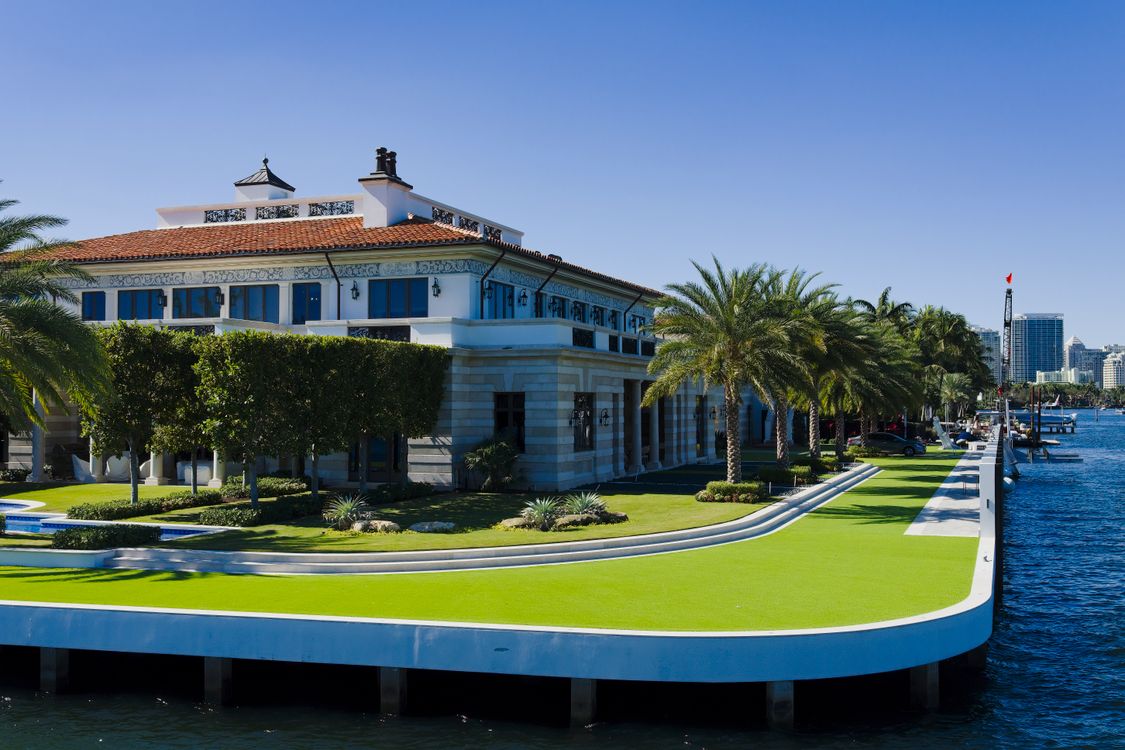White Mediterranean-style waterfront mansion with a manicured lawn and seawall on a South Florida waterway