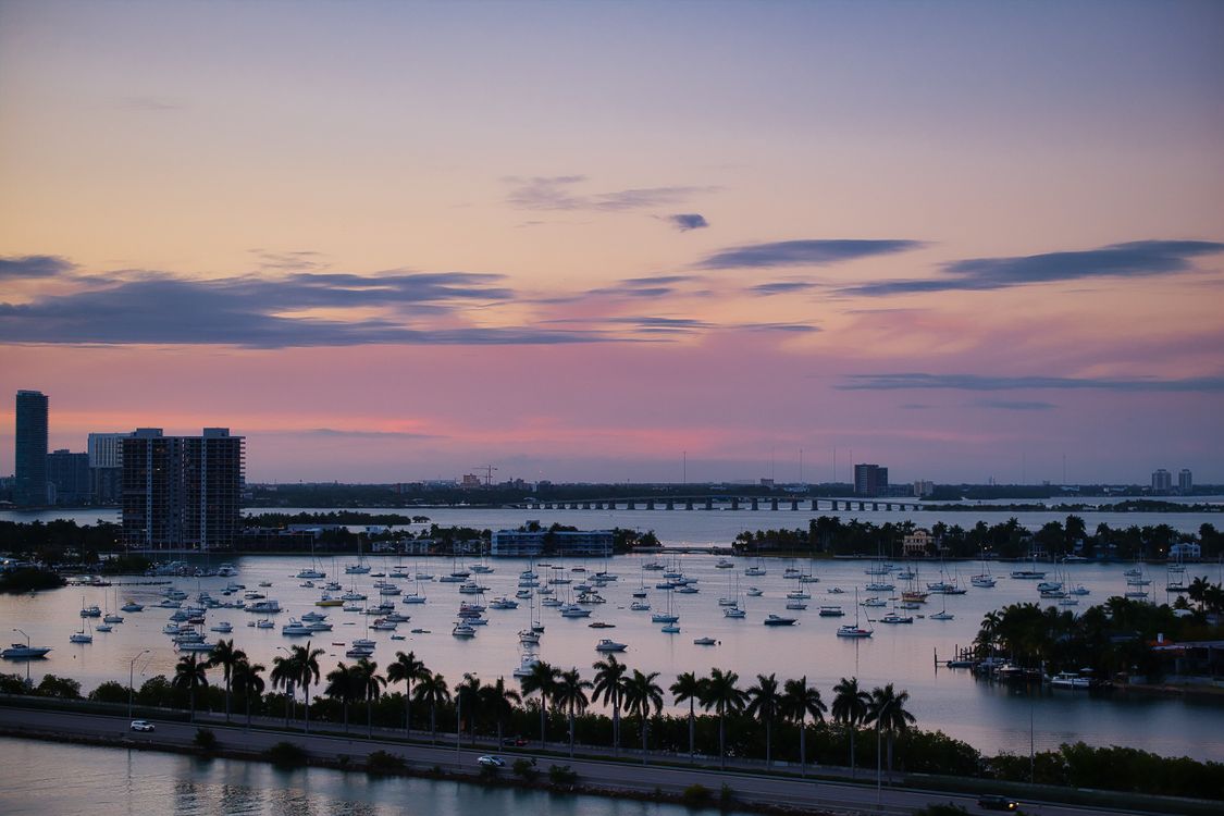 Biscayne Bay mooring field full of sailboats with the Miami skyline and a causeway at twilight