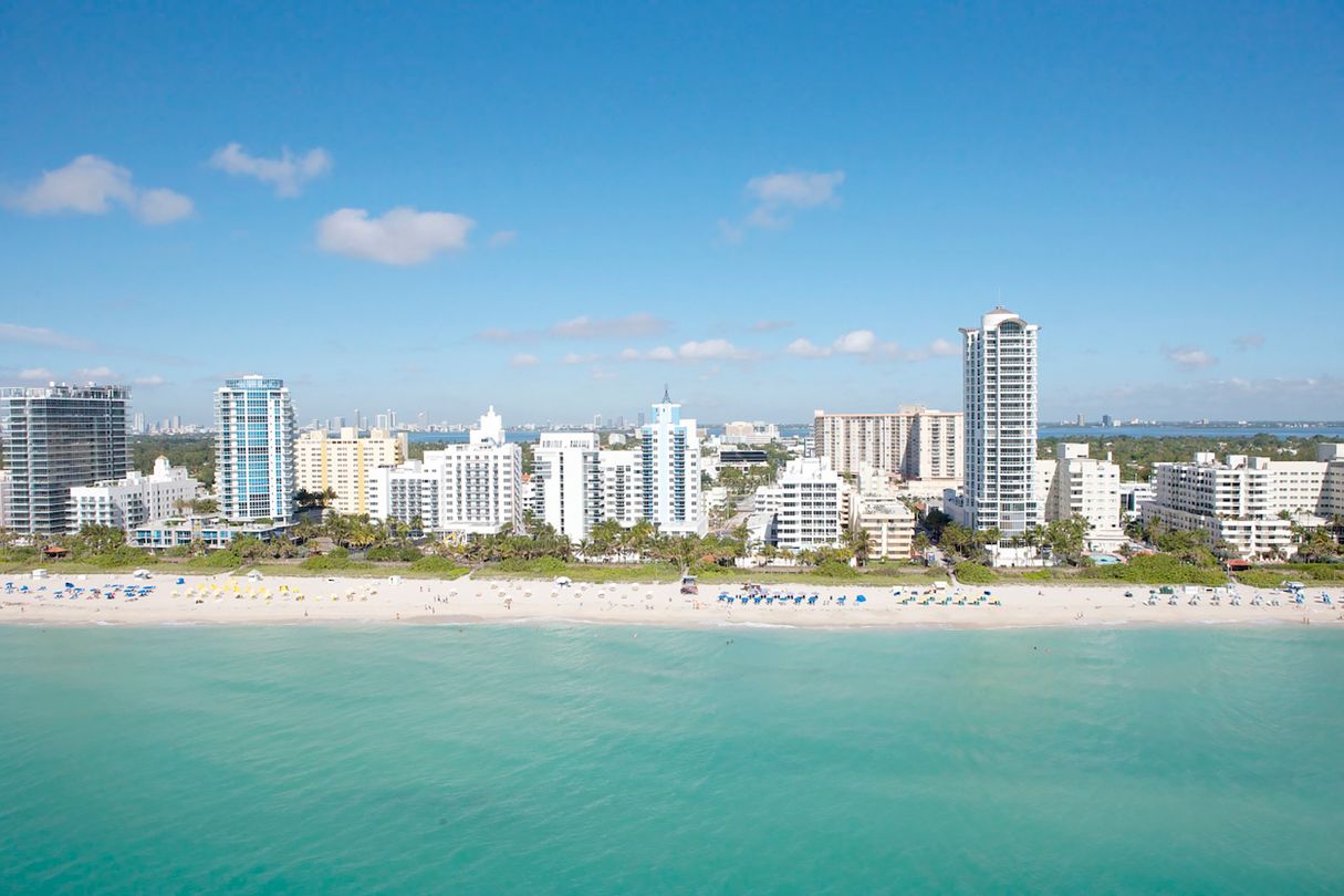 Vista aérea da parede de torres de condomínios à beira-mar de Miami Beach com o skyline de Miami ao fundo