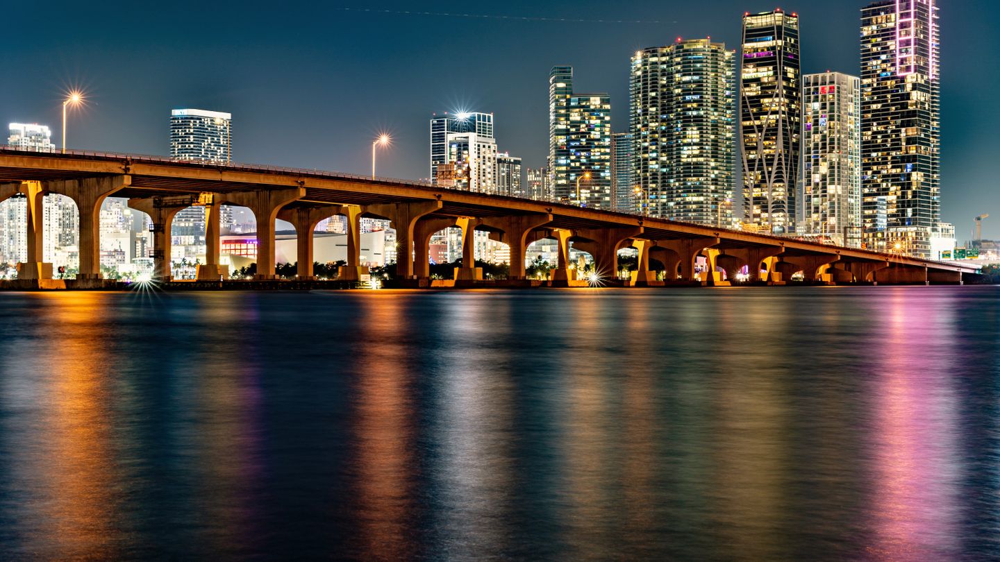 Venetian Causeway iluminado sobre a Baia de Biscayne com o horizonte de condominios do centro de Miami a noite em 2026