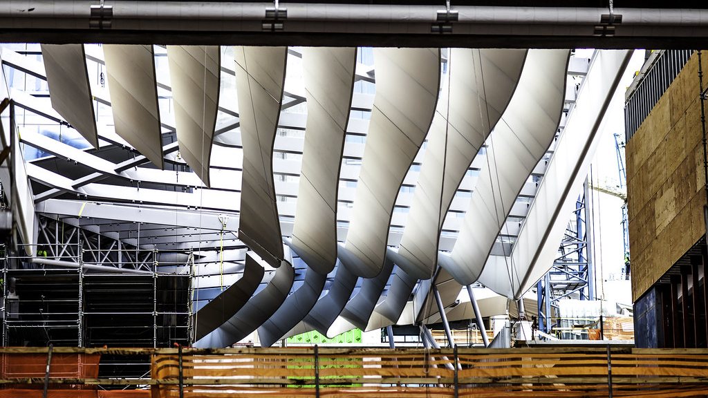The underside of a curved canopy structure under construction in Brickell, Miami, with scaffolding, site barricades and a crane behind it