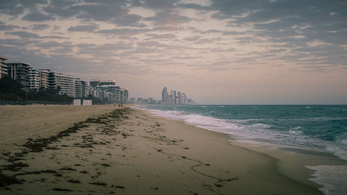 Surfside shoreline at dawn looking north toward the Sunny Isles Beach tower line, the oceanfront corridor holding the St. Regis and Bentley branded projects