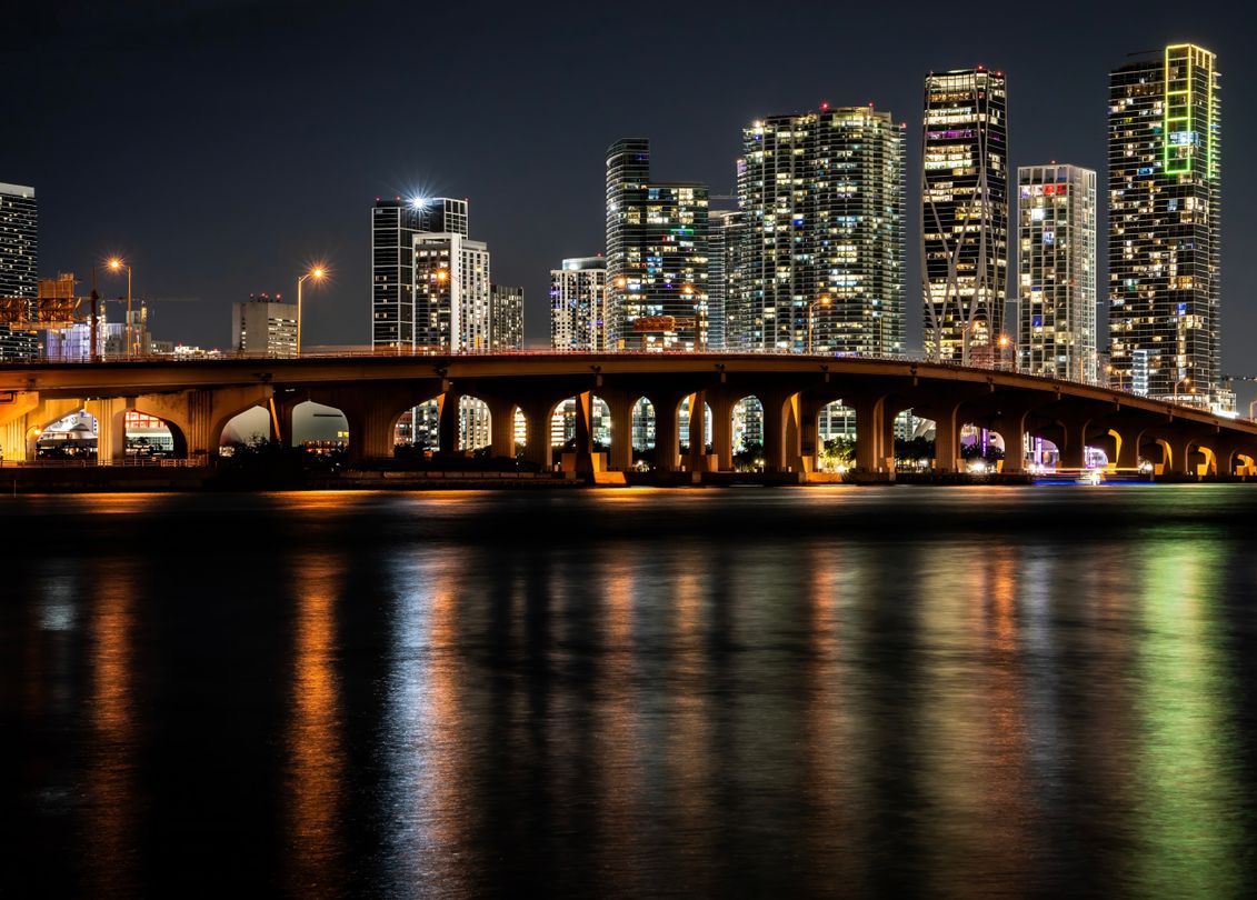 Downtown and Edgewater Miami condo towers lit at night across Biscayne Bay, the corridor holding most of the city's branded residence pipeline