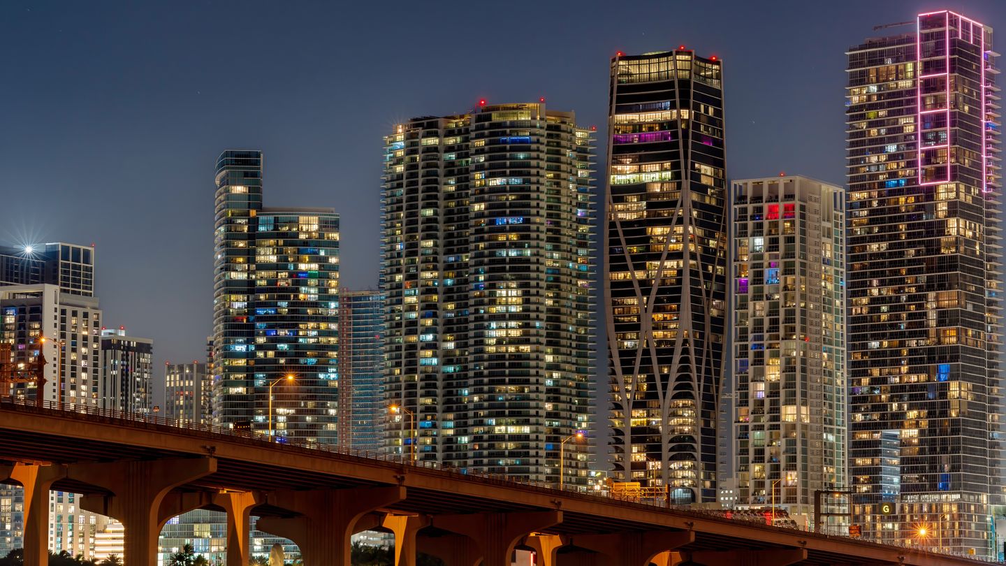 Downtown Miami condominium towers lit at night including One Thousand Museum, seen past the causeway