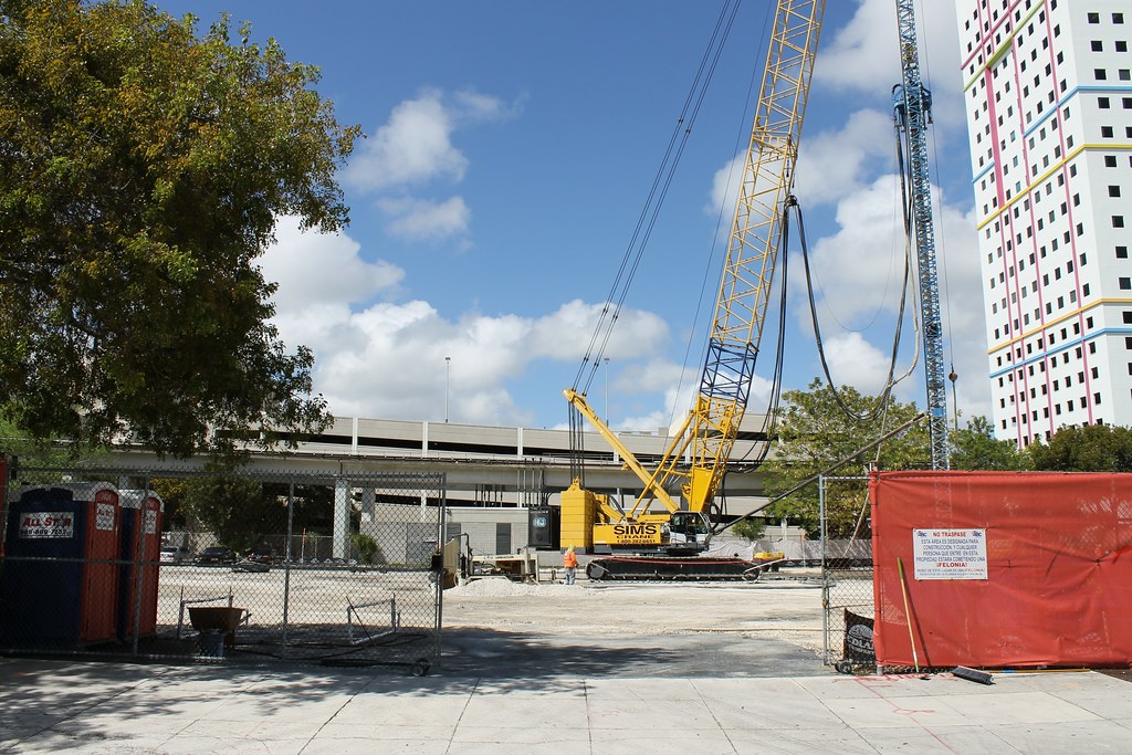 A fenced construction site with a crawler crane in Downtown Miami, a residential tower rising behind it