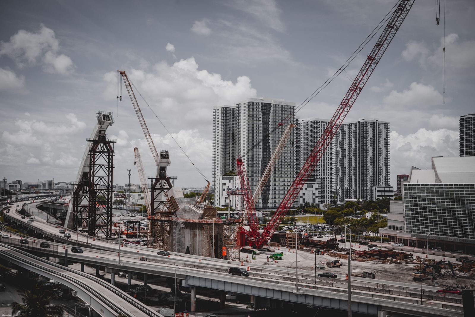 Construction cranes rising among high-rise buildings in a city under a cloudy sky